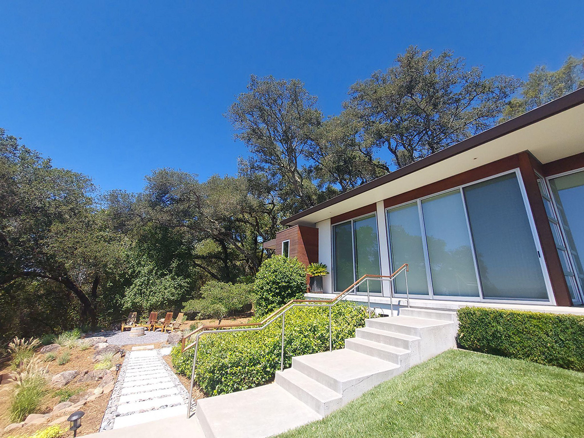 Home With Large Windows And Walkway To A Seating Area Outside 