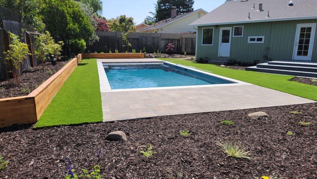 backyard with pool, green grass and plants next to a house