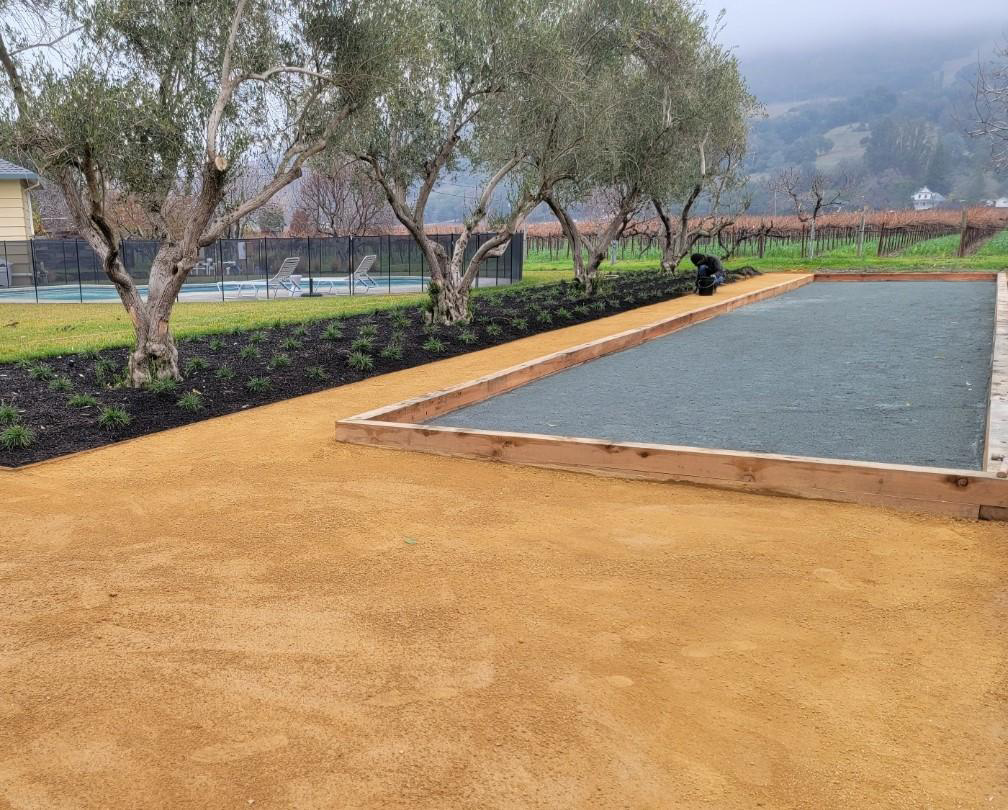 Large grey Bocce Ball court, trees, and vineyards in the background