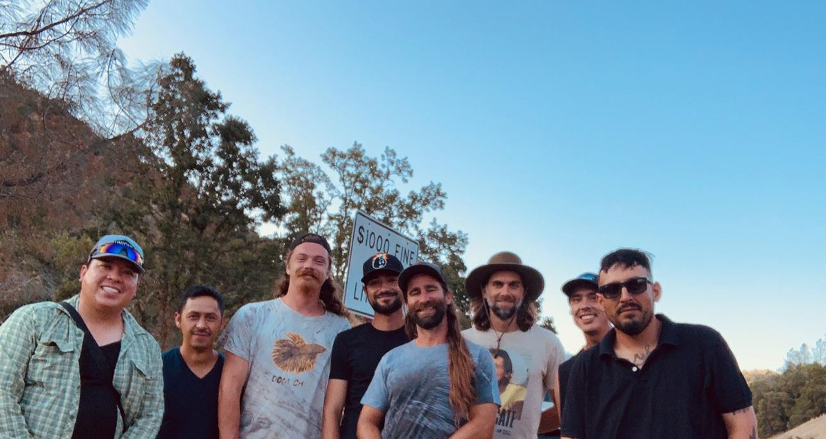 eight men smiling with trees and blue skies behind