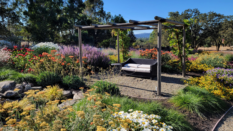 A rustic gazebo and seating area surrounded by blooming flowers and plants.