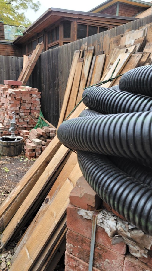 A jobsite with piles of materials laying around that were reused instead of dumped off site, including bricks, fenceboards, and drainage pipe.