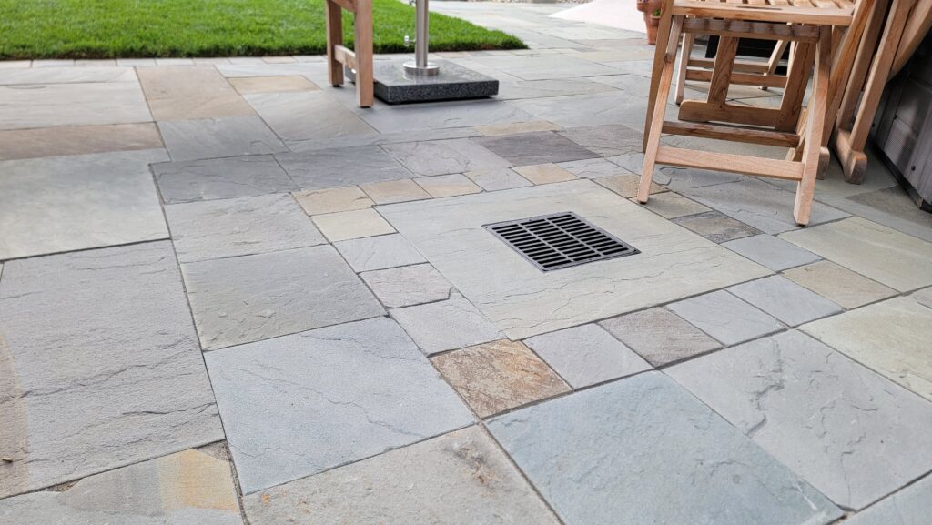 A bluestone paver hardscape installed by Inspired Landscapes with an area drain leading to an underground dry well in Fountain Grove. 