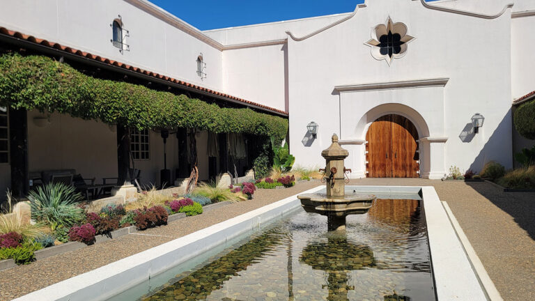 A large pond feature with water fountain surrounded by beautiful landscaping.