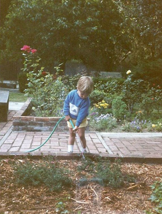 Boy outside watering plants.