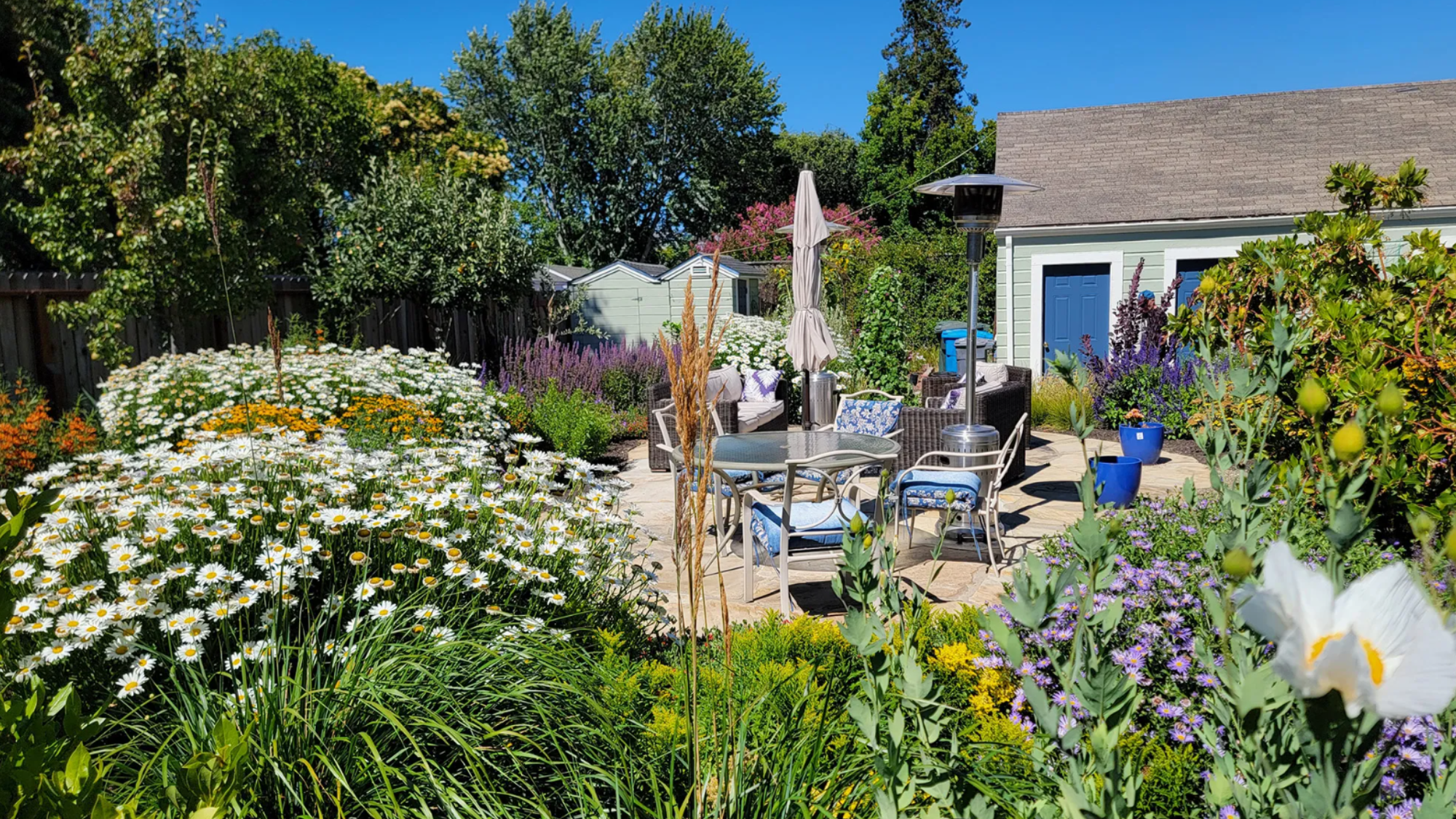 chairs, a table, and umbrella surrounded by lush pollinator-friendly plants.